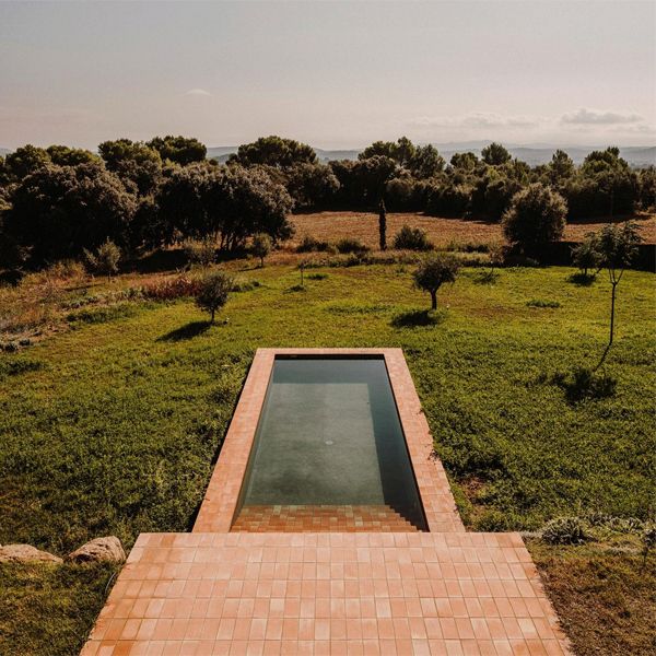 Vue sur la piscine Casa Ter, un projet Mesura en pleine campagne. Une piscine au design rectangulaire classique dans laquelle la brique occupe une place centrale, tant à l'intérieur qu'à l'extérieur, dans une élégante maison de style rustique