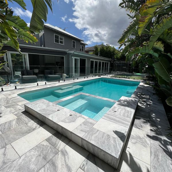 Rénovation élégante de piscine avec spa intégré, par Revival Pools, avec une combinaison de revêtements; carreaux en verre et pebbletec blanc et pierre extérieure de tons gris