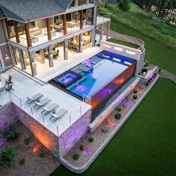 Vue aérienne spectaculaire d'une piscine à débordement de luxe, avec spa intégré, depuis Signature Luxury Pools, éclairée par des spots LED, au crépuscule