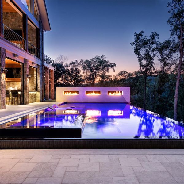 piscine à débordement, effet miroir, avec spa intégré, de Signature Luxury Pools, éclairée la nuit et avec petits foyers sur le mur extérieur